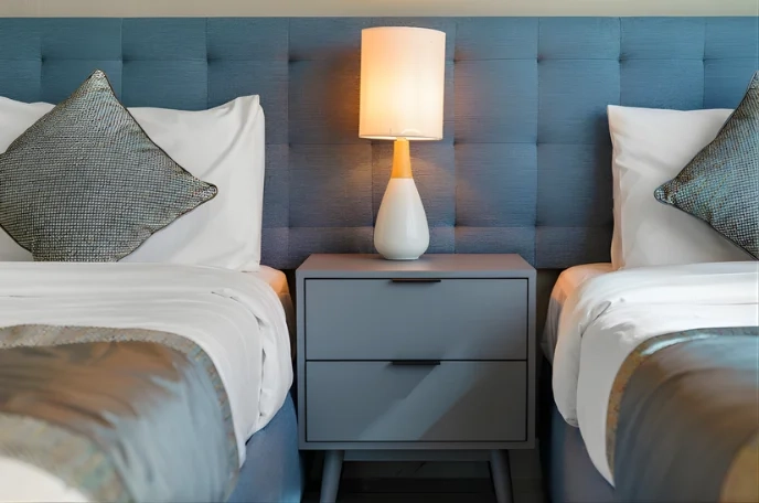 Twin beds with tufted blue headboard and bedside lamp